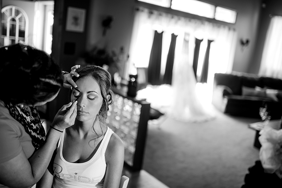 Bride getting her make up done with dresses hanging in background