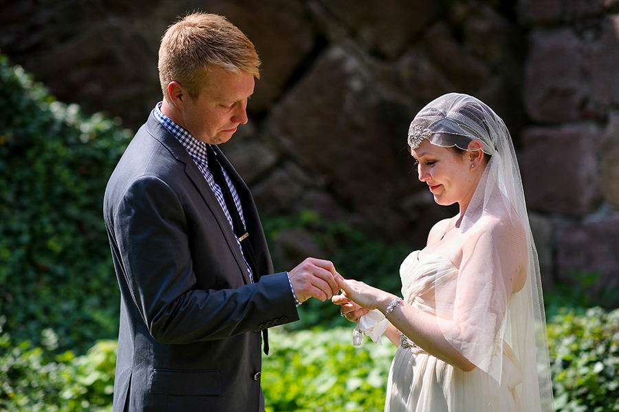 Groom places ring on brides finger during outdoor wedding ceremony.
