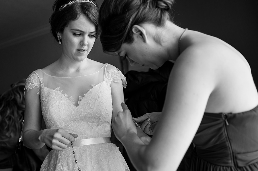 Bride's sister and maid of honor helping bride with wedding jewelry.