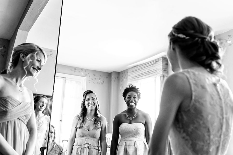 Bridesmaids reacting excitedly to bride in her dress on her wedding day.