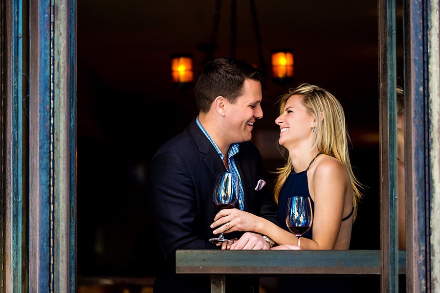 Engaged couple laughing while sipping wine in an 