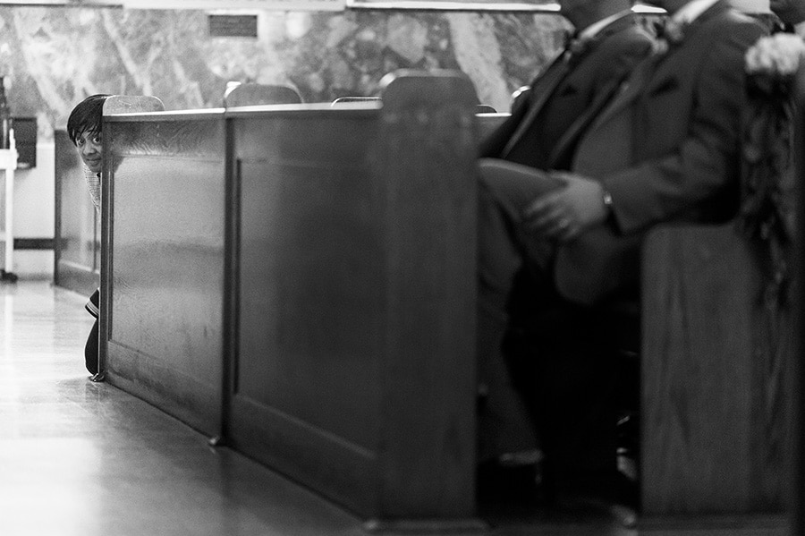 photographer peeking around pew in church.