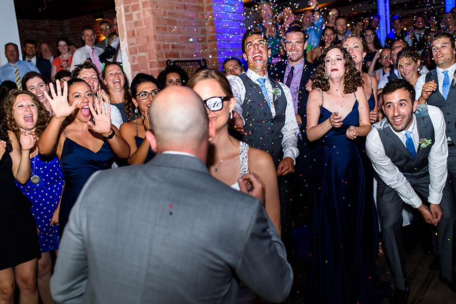Weddings guests throw confetti at bride and groom as they enter reception.