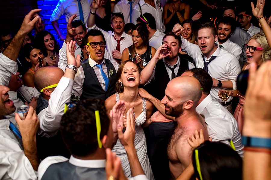 Bride and guests react to shirtless groom singing during wedding reception.