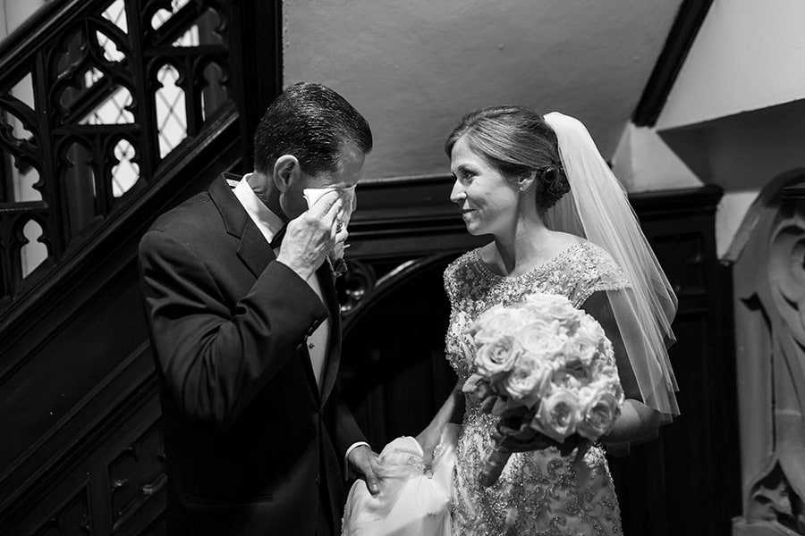 Bride looks at her father wiping tears away before wedding ceremony.