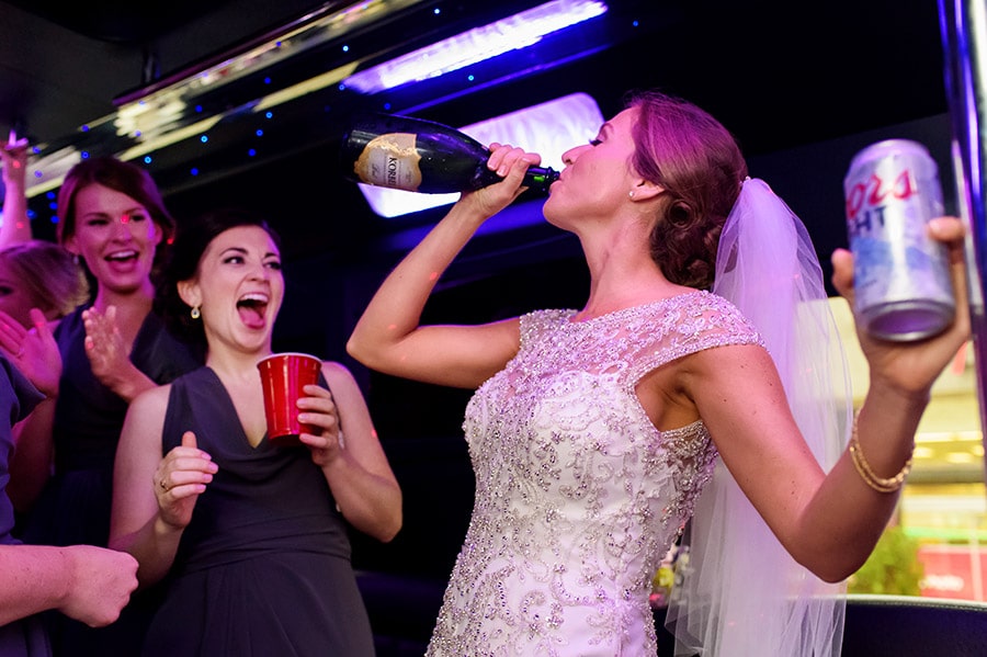 Bride chugs champagne on bus after wedding ceremony.