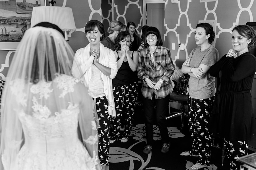 Mother of the bride and bridesmaids laugh and cry as they see bride in her dress for the first time.