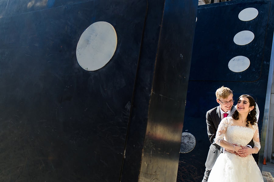 Bride and groom snuggling on giant domino game pieces in Philadelphia park near City Hall.