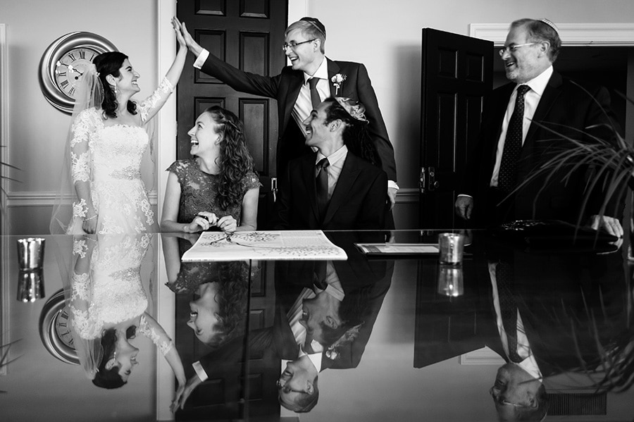 Excited bride and groom high-five as witnesses sign their Ketubah, a Jewish wedding tradition, during the wedding day.