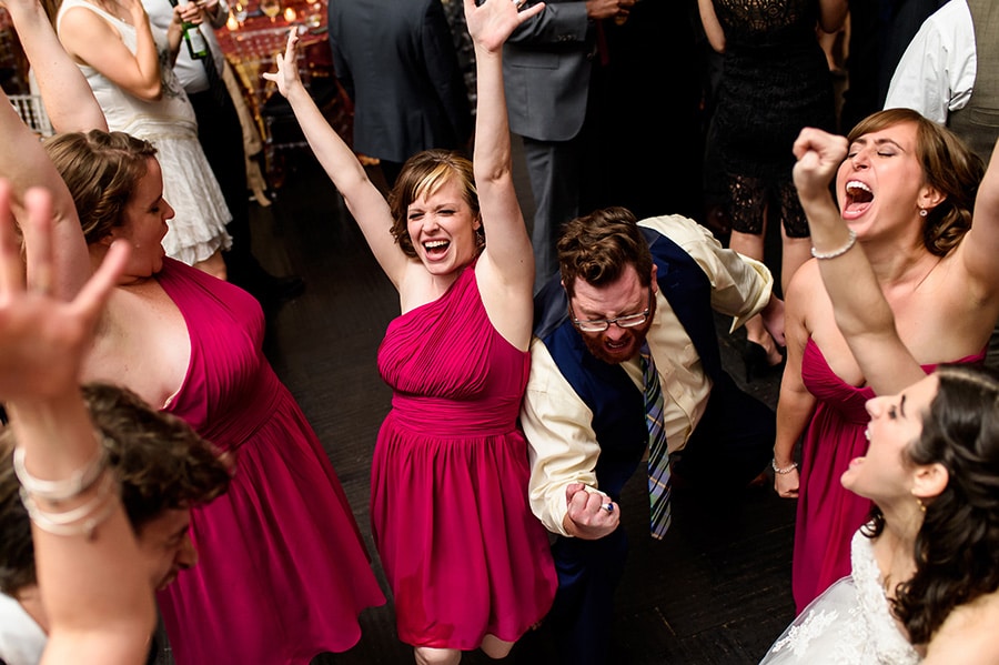 Bridesmaids and guests throw their hands up in the air as they dance during wedding reception.