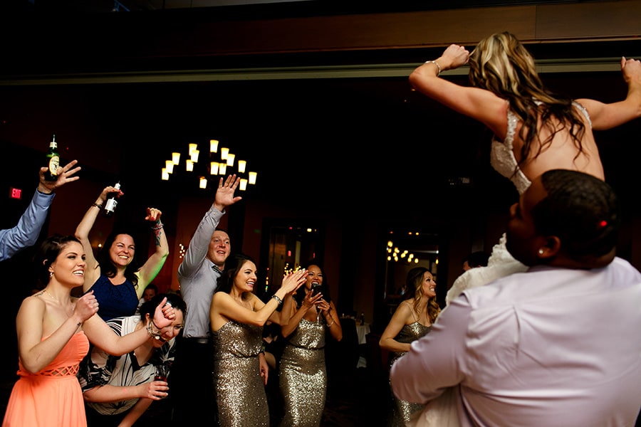 Wedding guests laugh and cheer as bride's friend lifts her on his shoulder during wedding reception at Bear Creek in Macungie, PA.